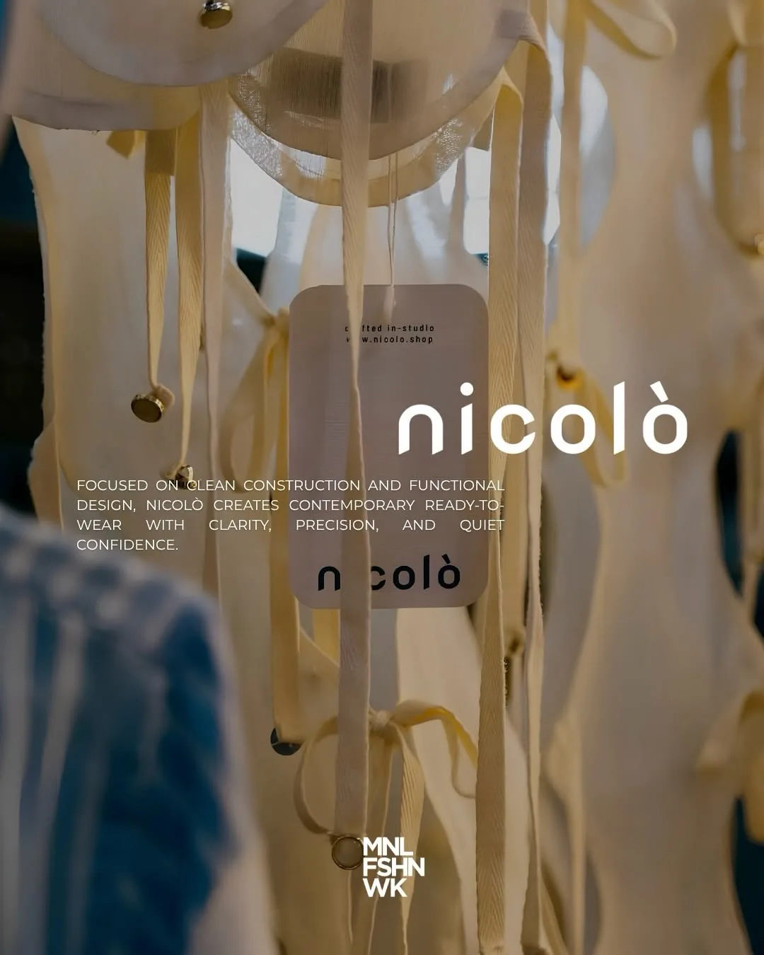 Garments and hang tags in the Nicolò studio between racks of unfinished pieces
